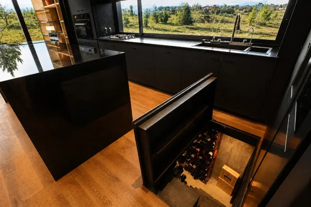 Surface Construcciones — Casa Nórdica (Trevelin, Patagonia), cava de vinos subterránea con acceso mediante trampa oculta en la cocina