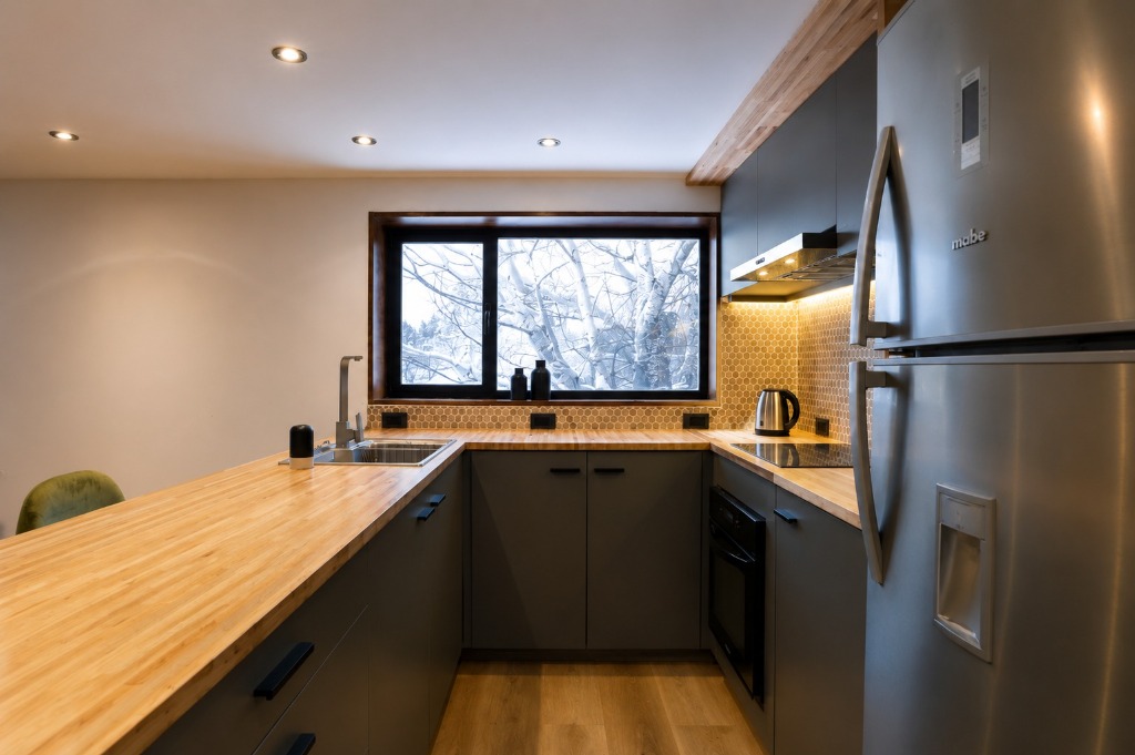 Surface Construcciones — Casa Huésped en Trevelin, cocina equipada en U con revestimiento hexagonal y ventana al bosque nevado