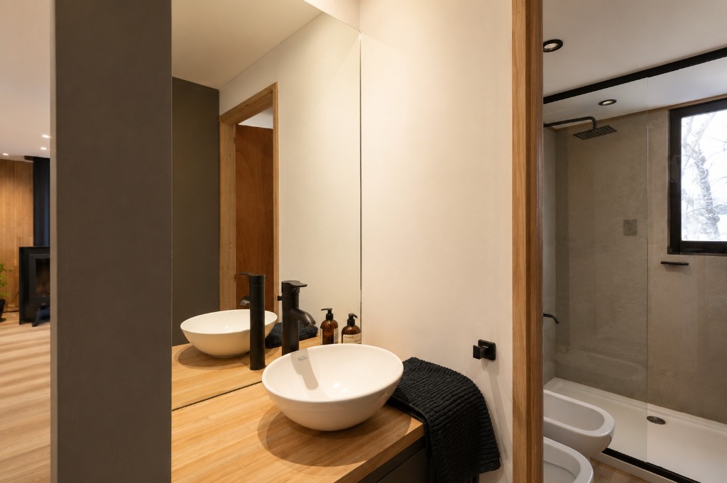 Surface Construcciones — Casa Huésped en Trevelin, baño completo con bacha de apoyo artesanal, grifería negra mate y mampara vidriada